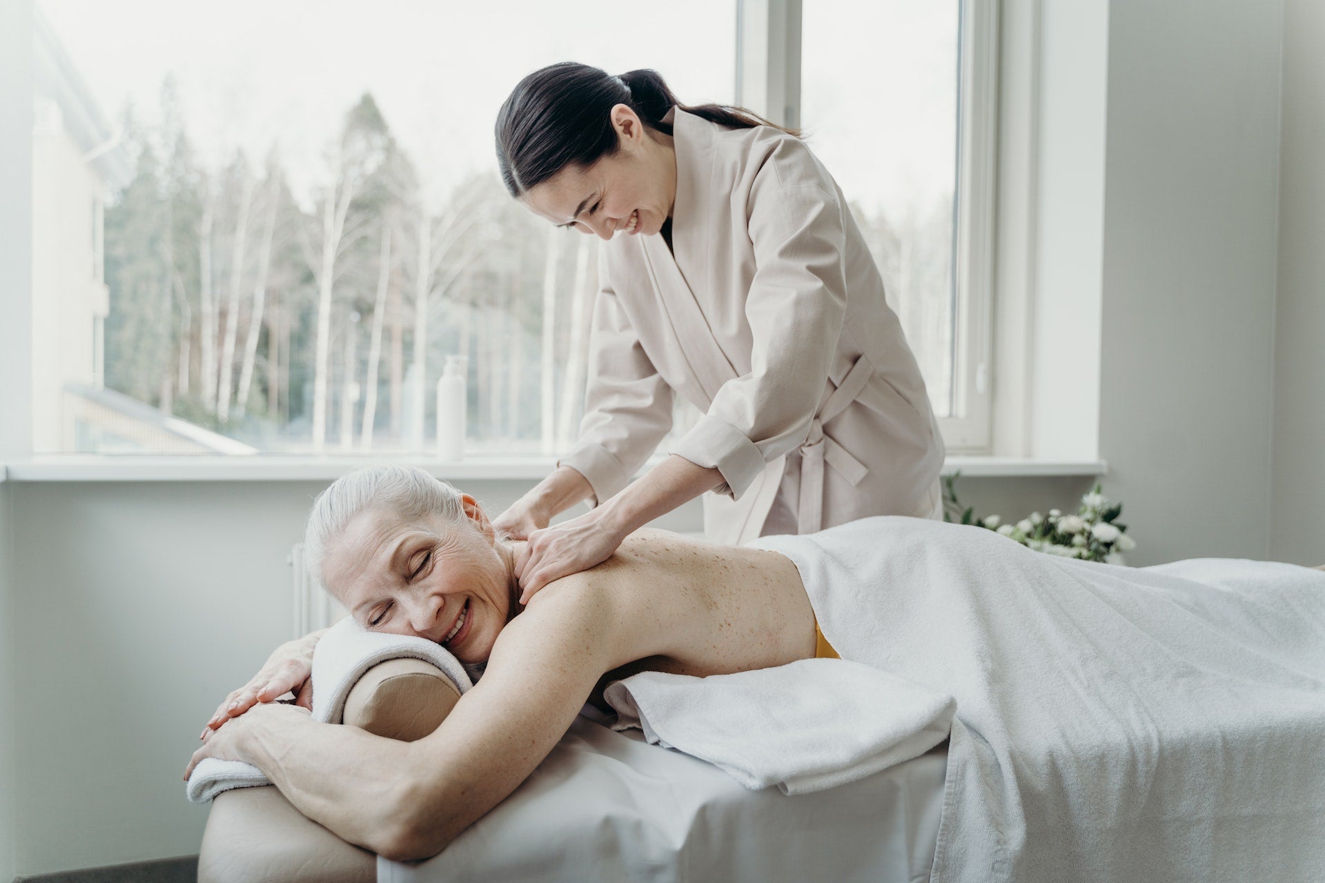 Home spa session: Smiling old woman enjoying a professional massage therapy at home.