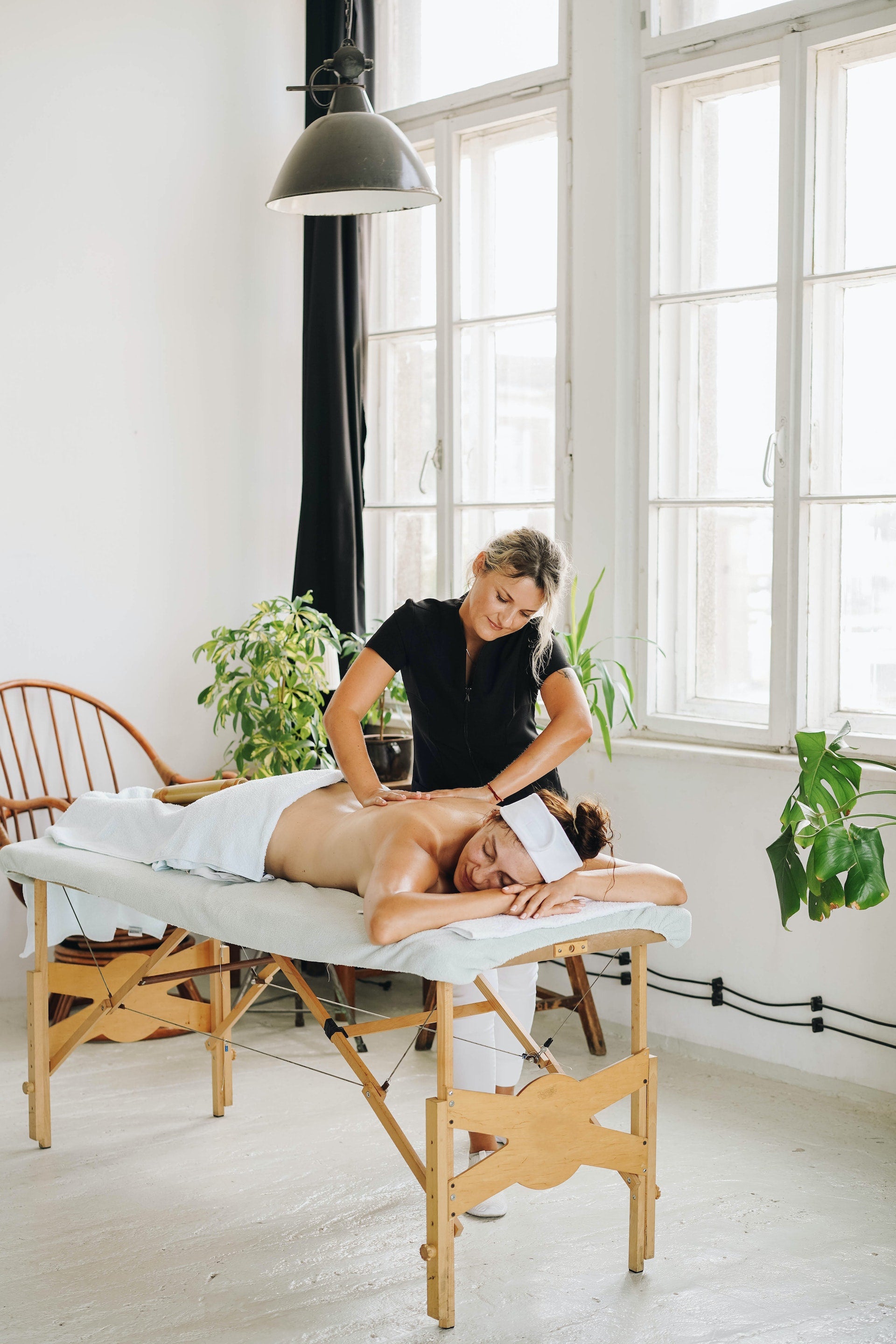 Home spa session: Woman enjoying a relaxing massage therapy at home made by therapist in black uniform.