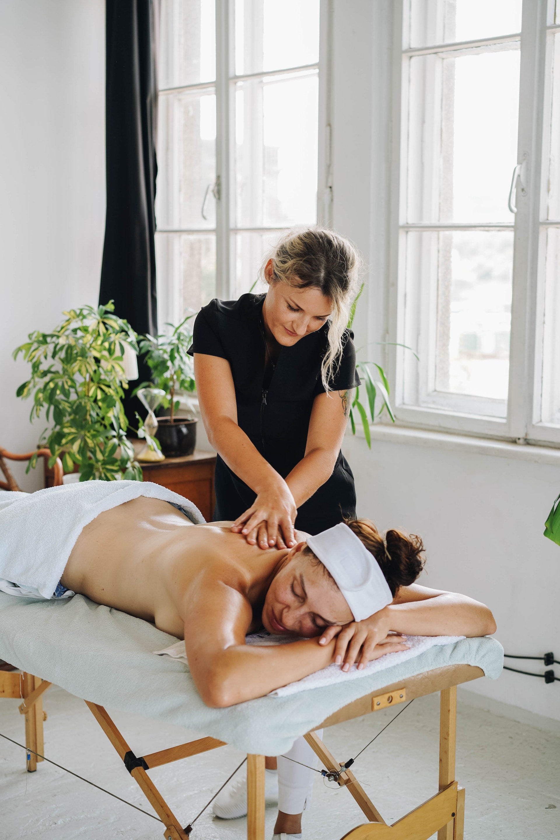 Home spa session: Woman enjoying a soothing massage therapy at home made by therapist in black uniform.