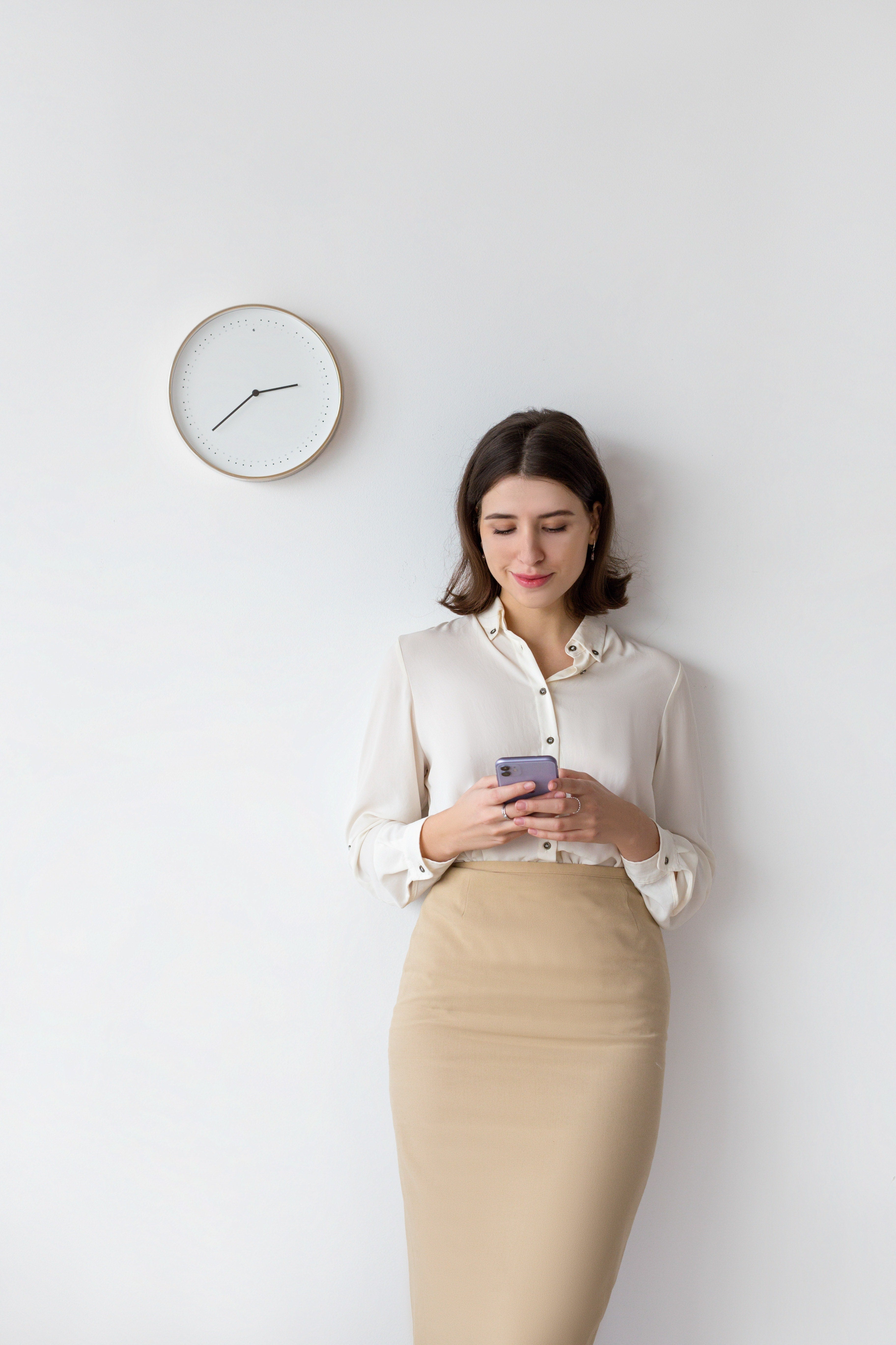 Woman with a phone against a wall with a clock beside her representing last minute booking