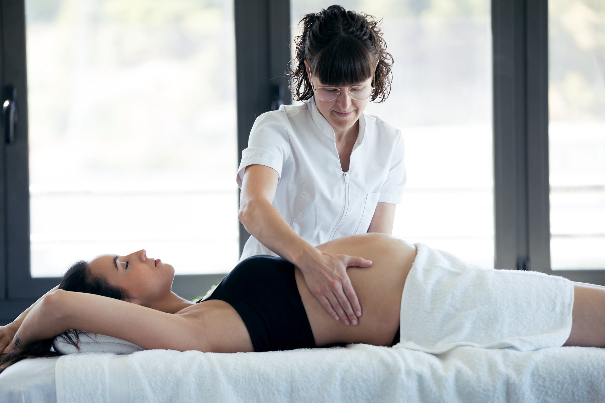 Home spa session: Pregnant woman enjoying a professional prenatal massage therapy at home.
